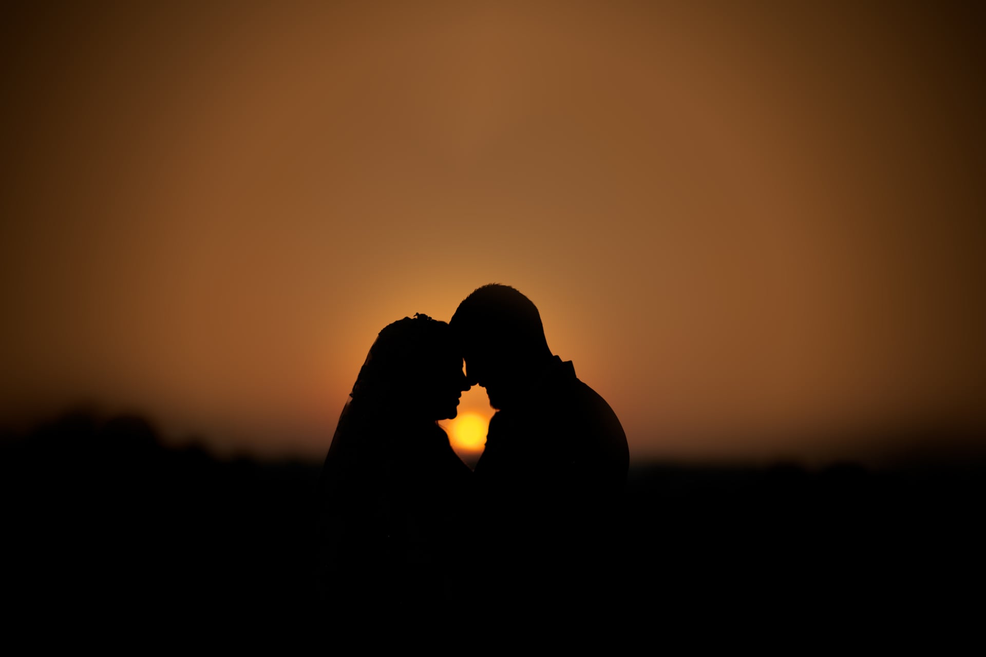 A bride and groom silhouetted against the setting sun.