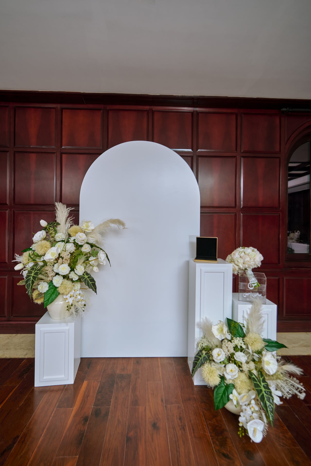 White floral arrangements and pedestals around an arched wedding backdrop.