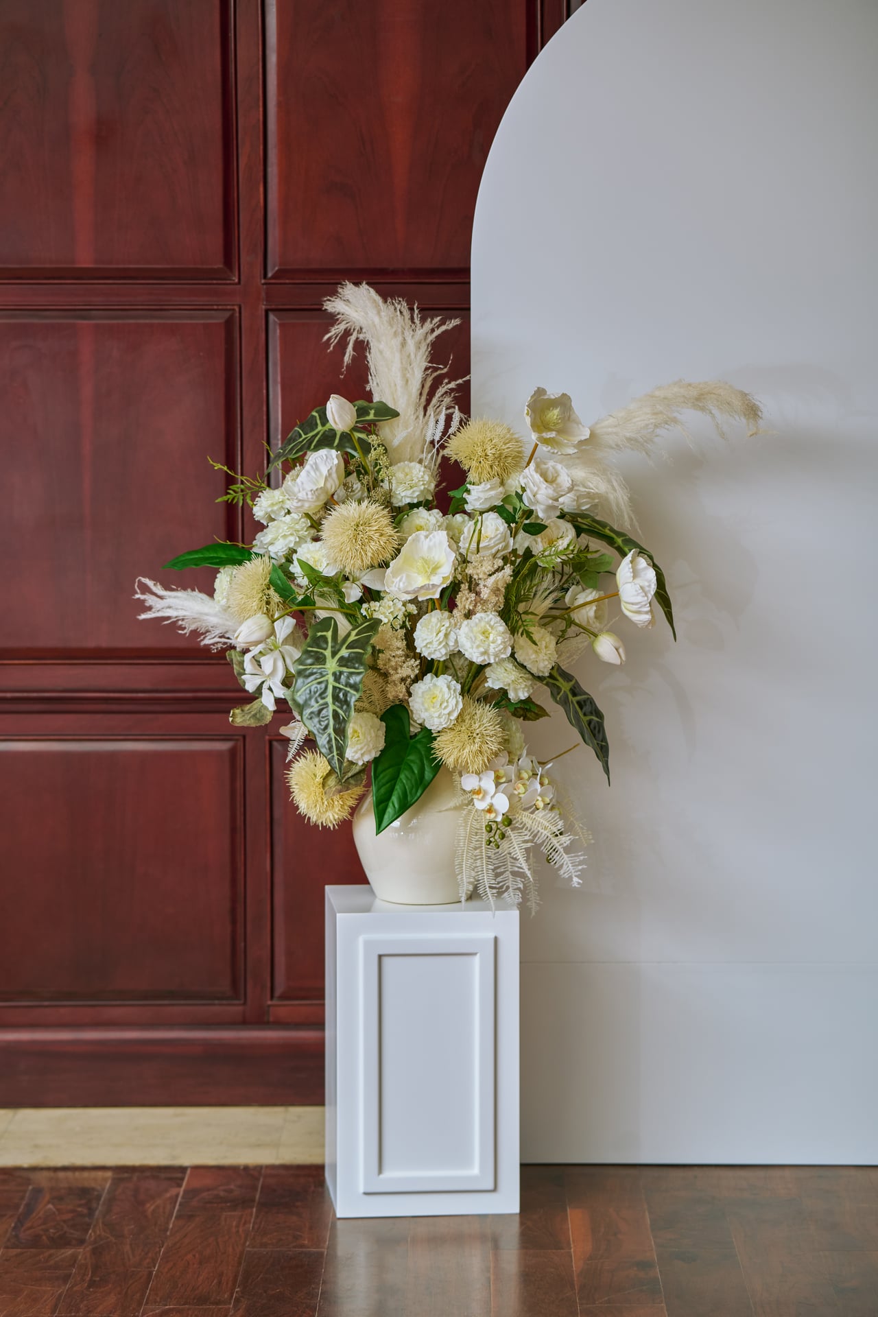 Ivory and green flowers in a vase on a white pedestal.